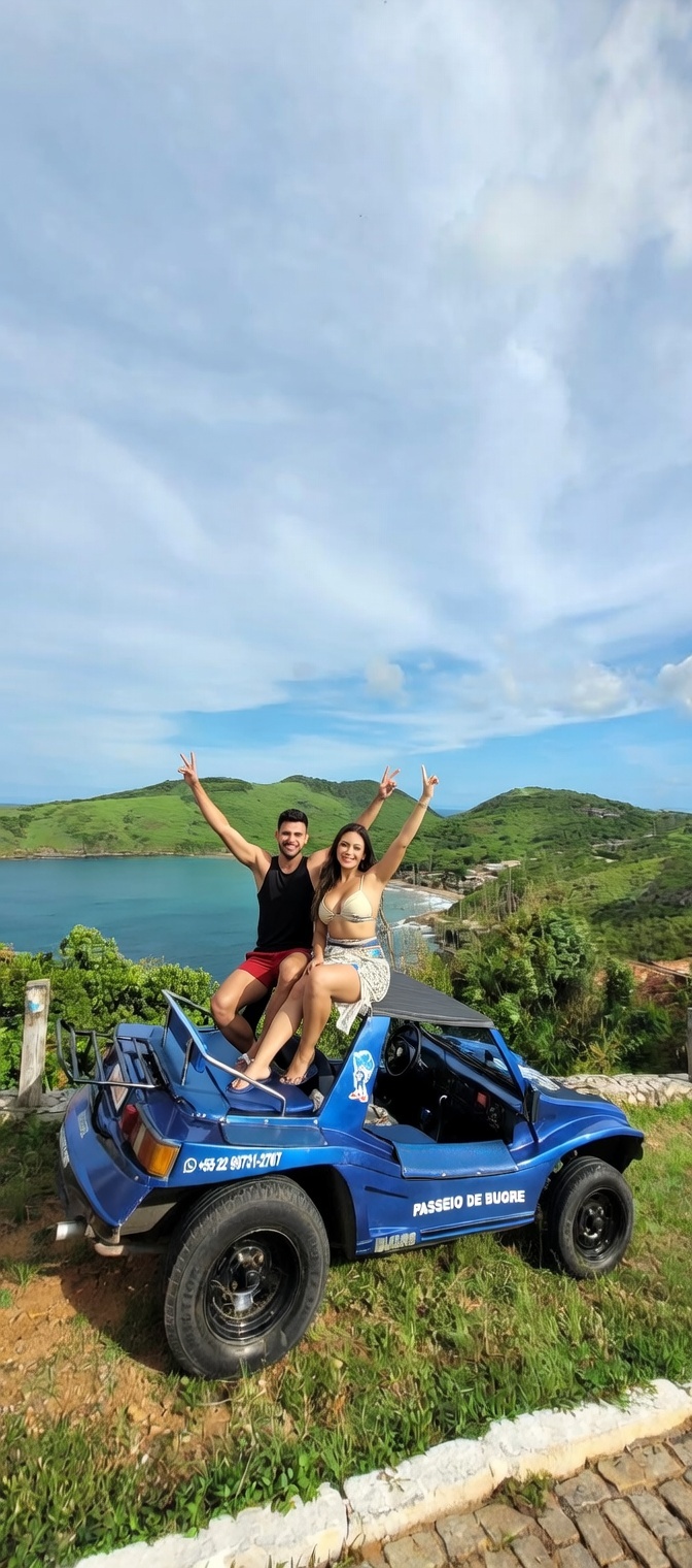 Um buggy azul estacionado em um mirante panorâmico em Búzios sob um céu dramático e nublado