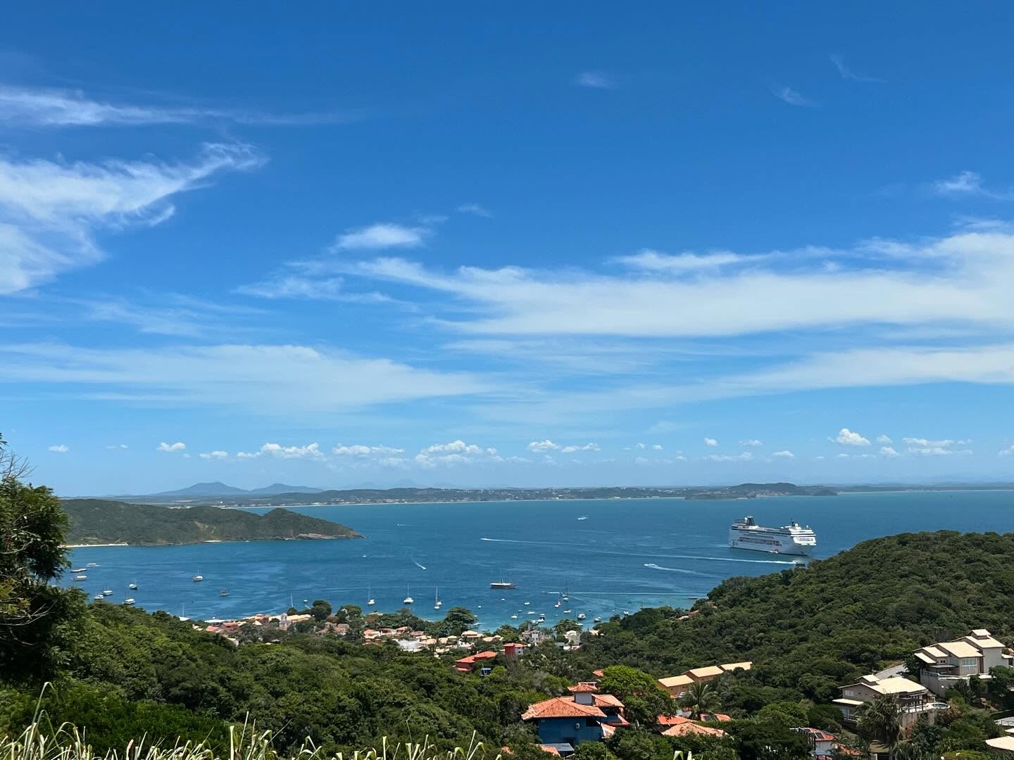 Vista panorâmica do alto da baía de João Fernandes com águas azul-turquesa, casas de luxo e a linha costeira de Búzios ao fundo.