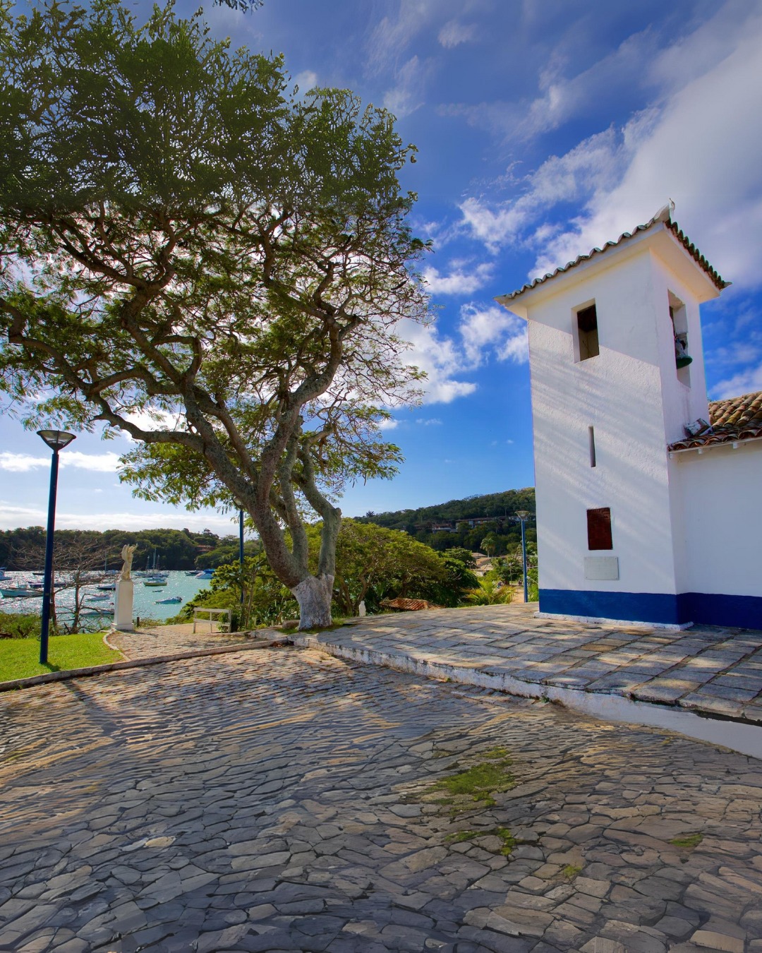 A histórica igreja branca de Sant'Anna com vista para o mar azul-turquesa e barcos de pesca coloridos em Búzios.