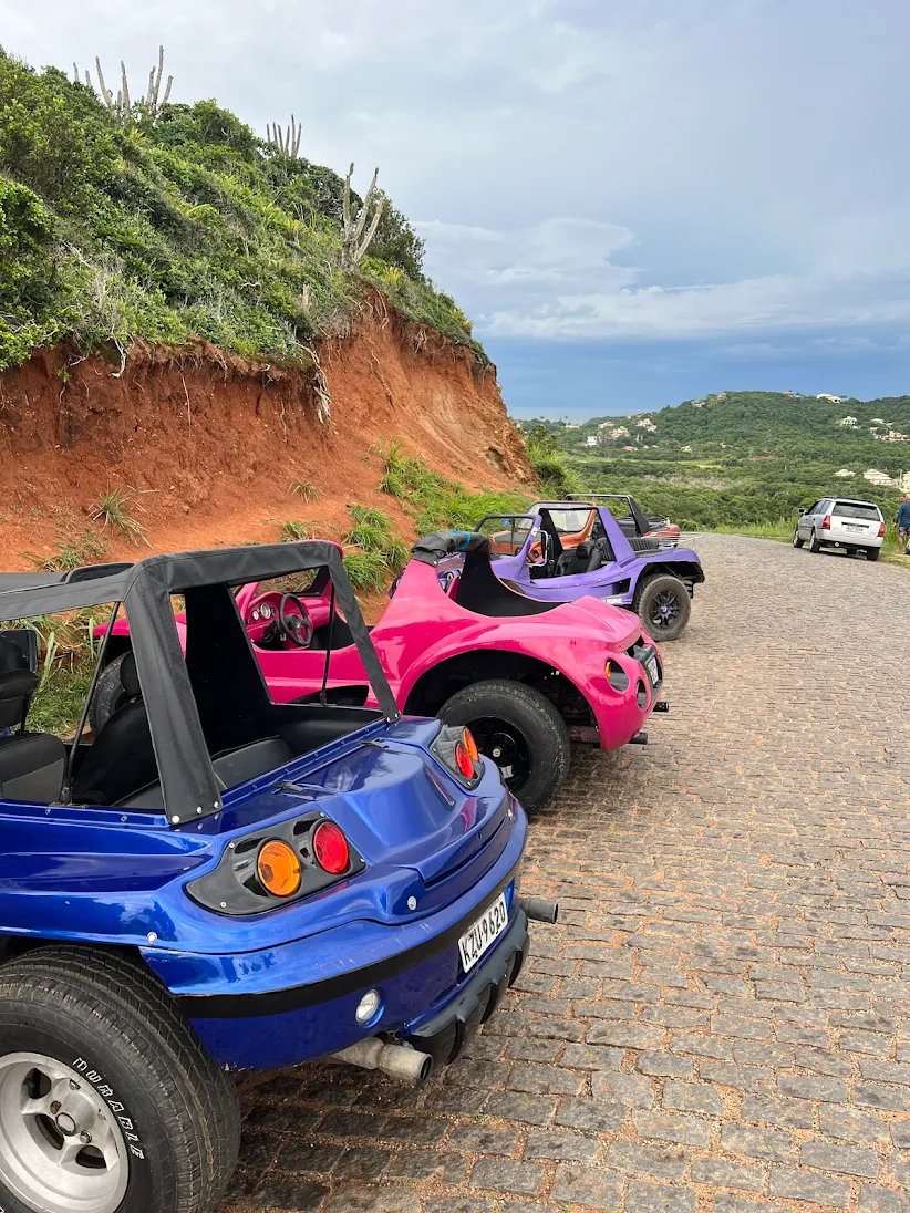 Um turista sorrindo enquanto olha para um smartphone com a tela de confirmação da Buggy Búzios, com a costa de Búzios ao fundo.