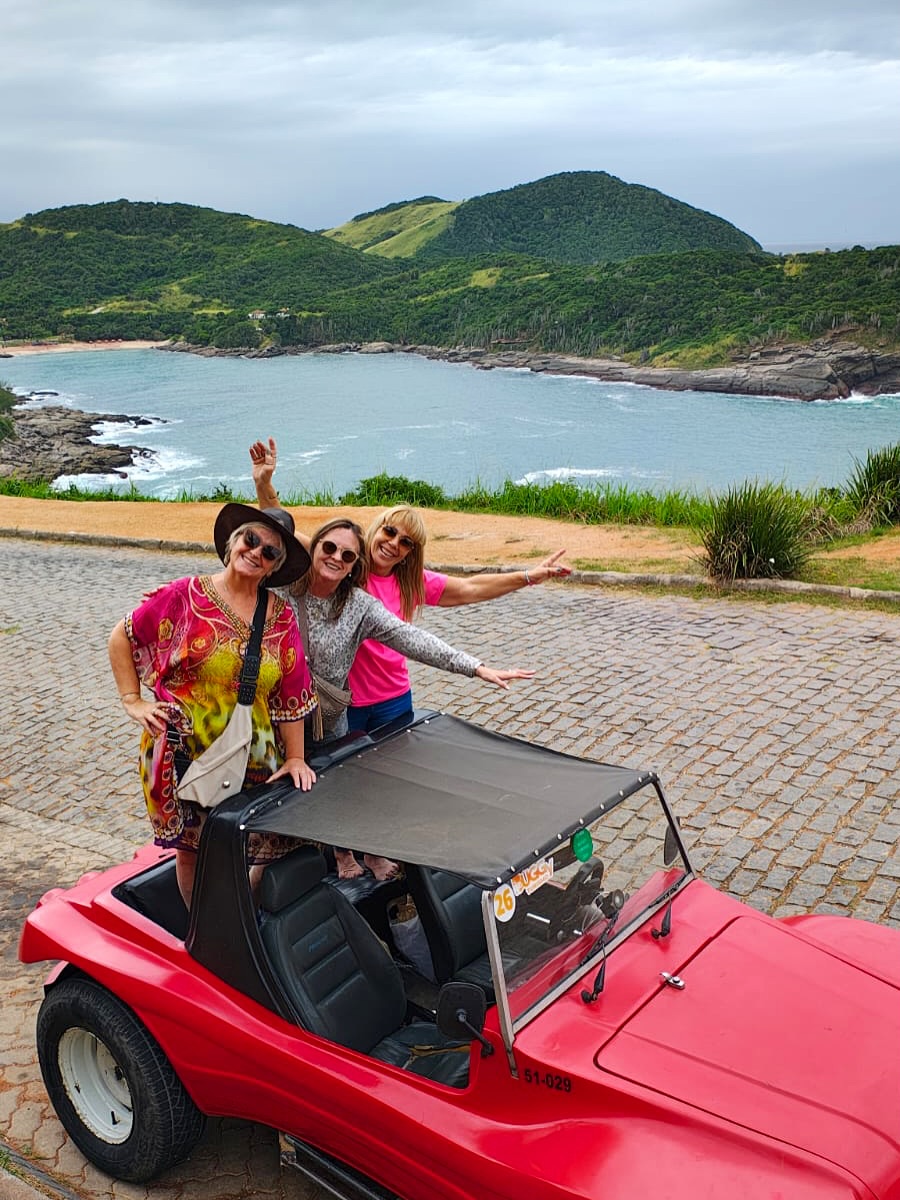 An open-air private buggy driving along the scenic coastline of Búzios on a dramatic, moody morning with a little rain and soft lighting over the ocean