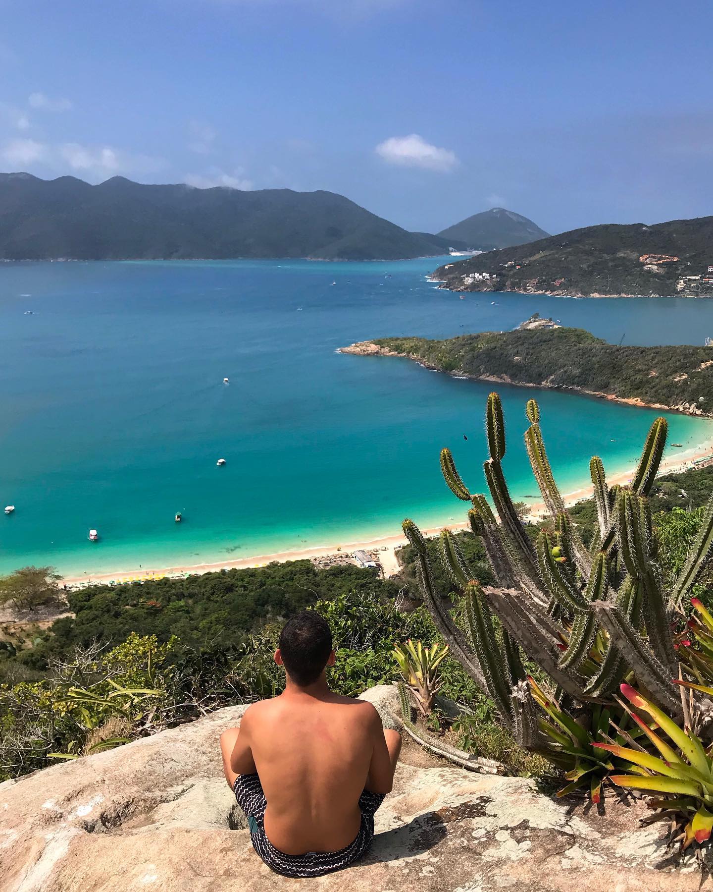 A comprehensive panoramic view of the Búzios coastline featuring buggies on the cliffs and boats navigating the crystal-clear ocean bays