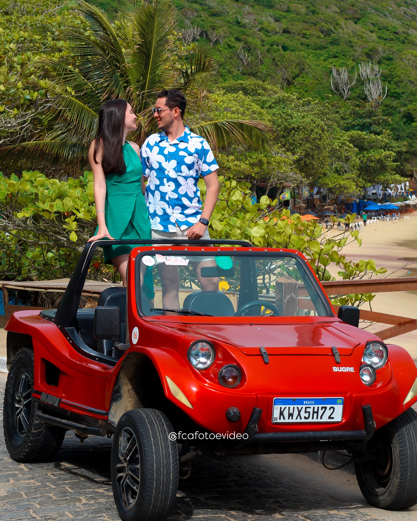 Pareja disfrutando de un buggy rojo de alquiler en un mirador de Búzios con vista al mar azul.